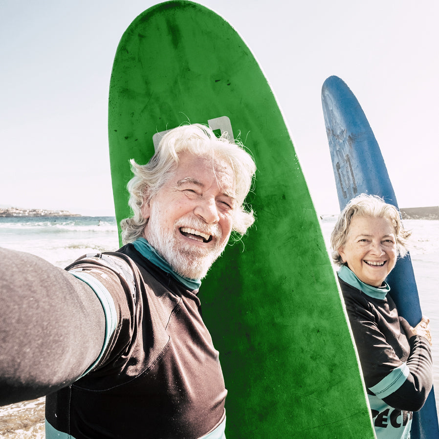 Zwei glückliche ältere Personen mit Surfboards am Strand